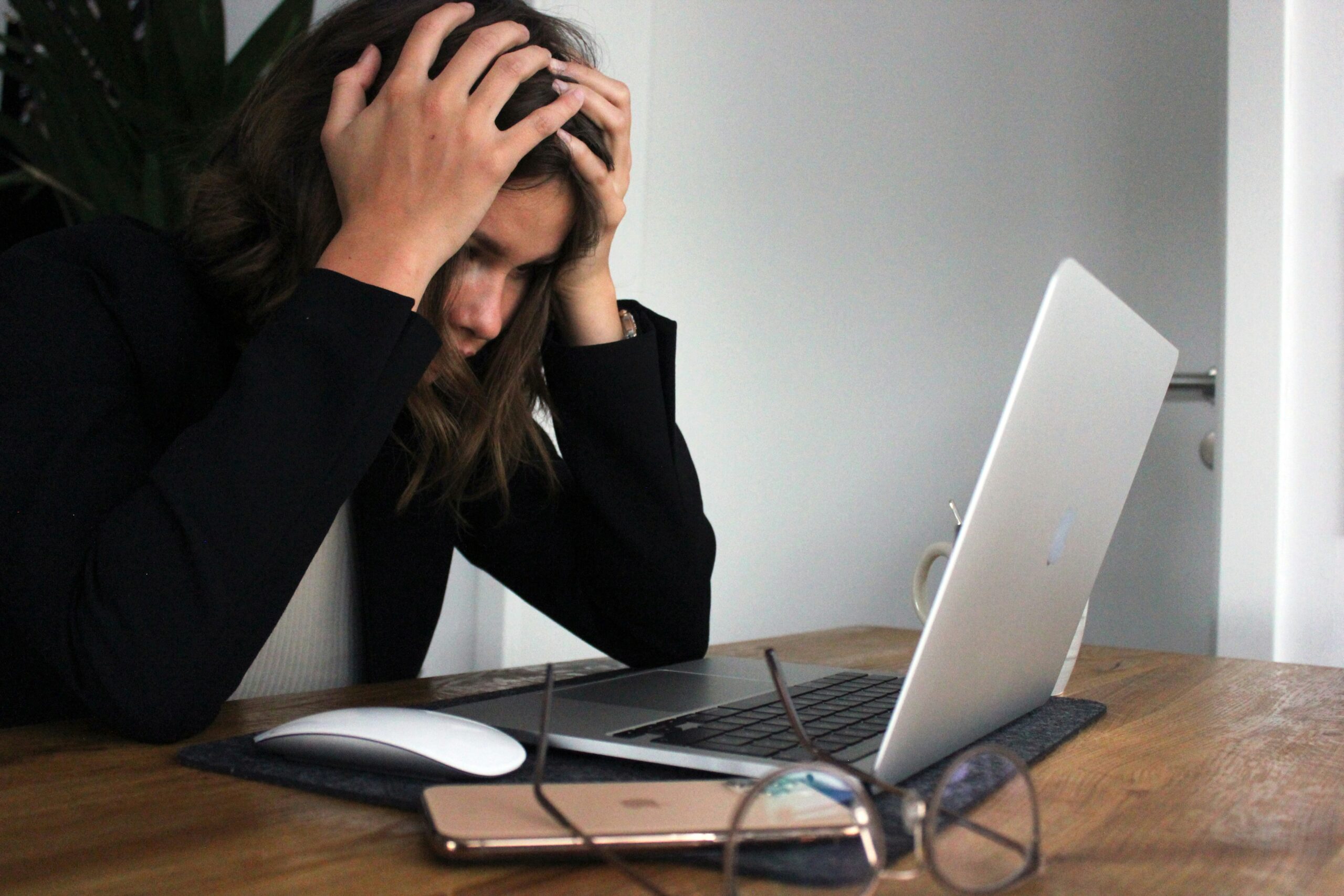 A woman grabbing her head in front of a laptop and burnout